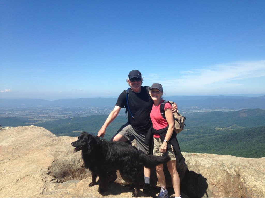 Mike & Sharon Adams with their dog. A view from the mountain they're on is in the background.