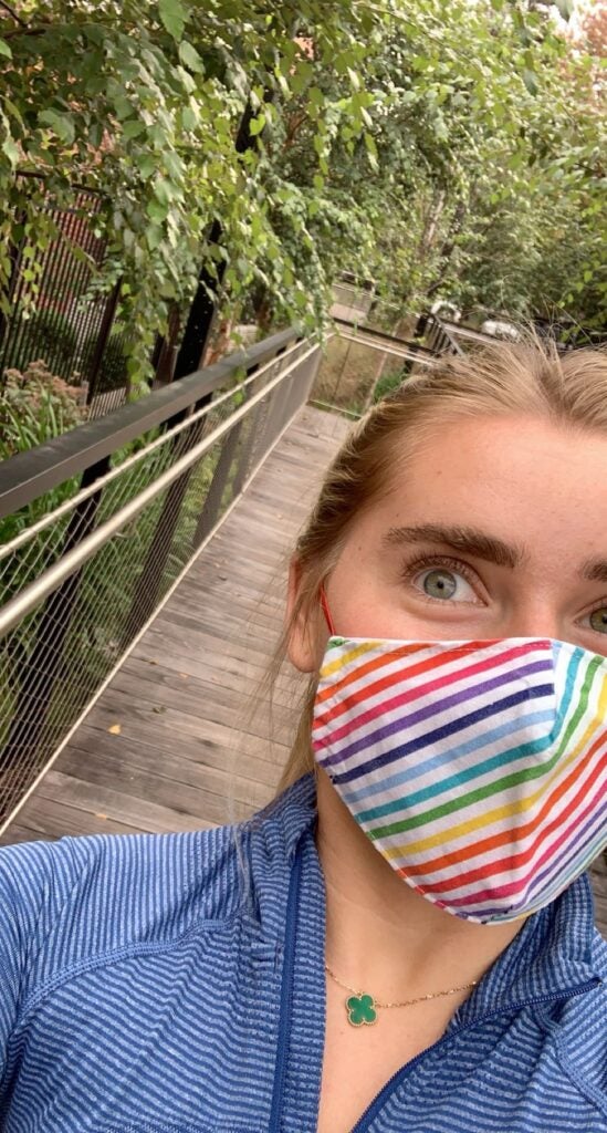 Selfie of Annabelle wearing a rainbow-striped face mask walking on a raised wooden walkway.