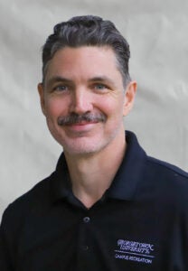 Man smiling in front of a gray background.